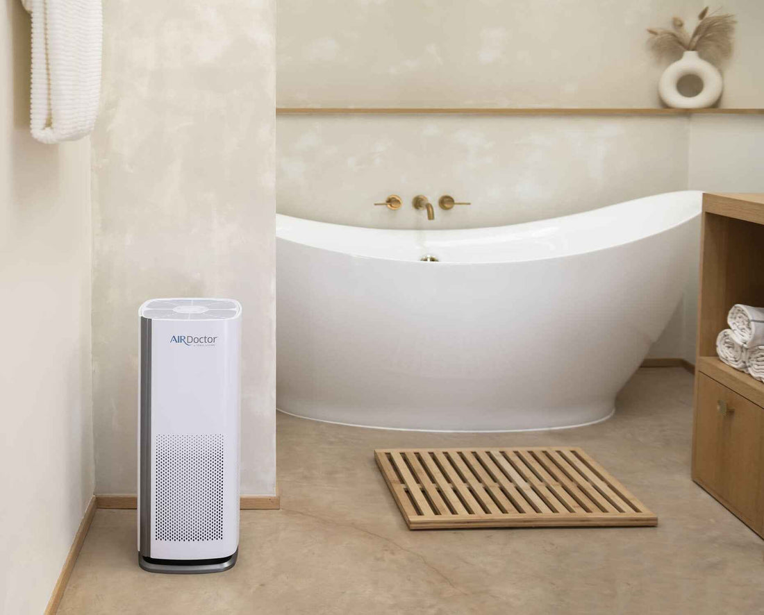 AirDoctor 1000 air purifier unit operating in a luxury bathroom near a soaking tub and wooden bath mat.