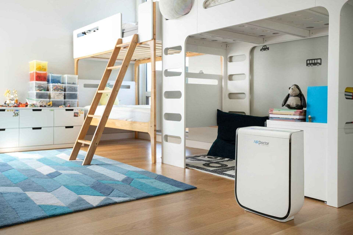 A white AirDoctor 2000 air purifier sitting on a wooden floor in a brightly lit children's bedroom.