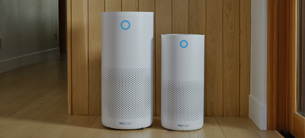 AirDoctor 4000 and AirDoctor 1500 Air Purifiers standing against a wall facing the camera with their indicator lights showing that the home has good air quality.