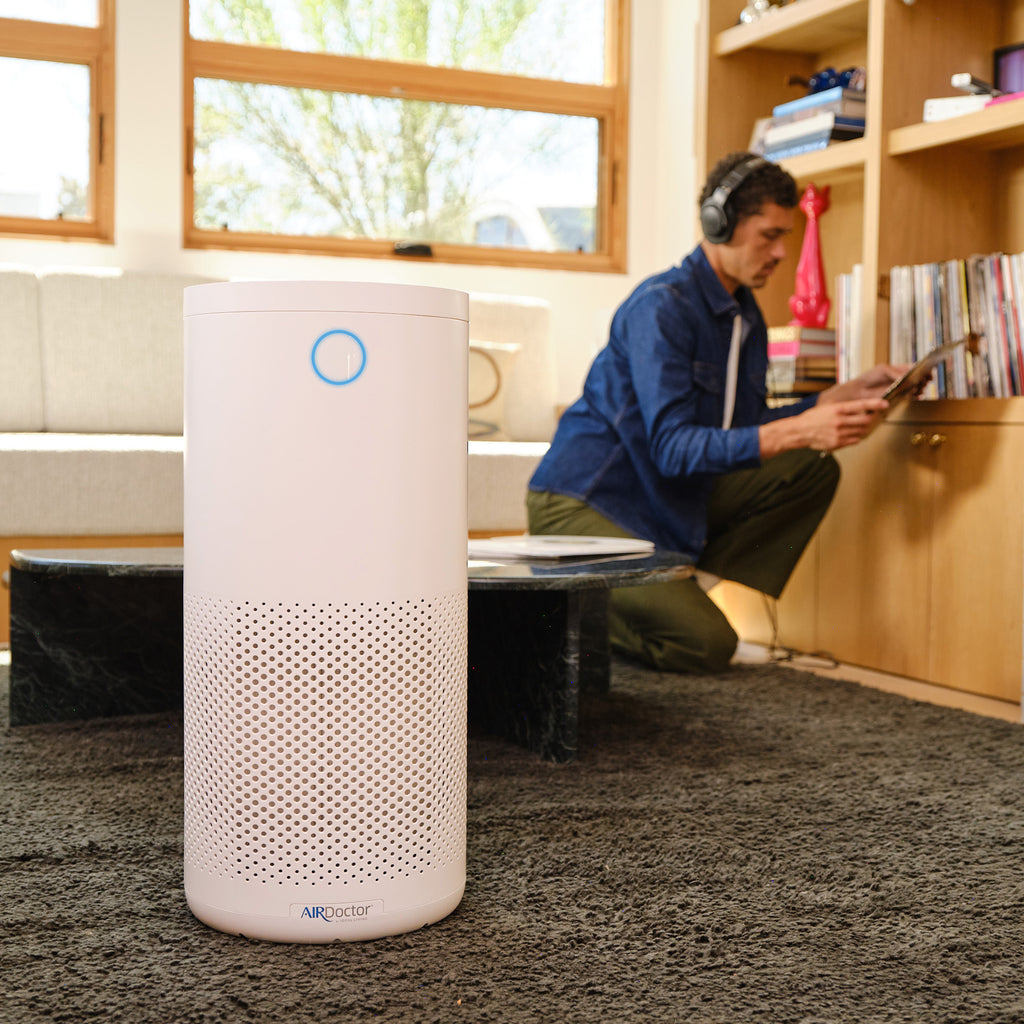 An AirDoctor 1500 in a living room with a man listening to vinyl records in the background.