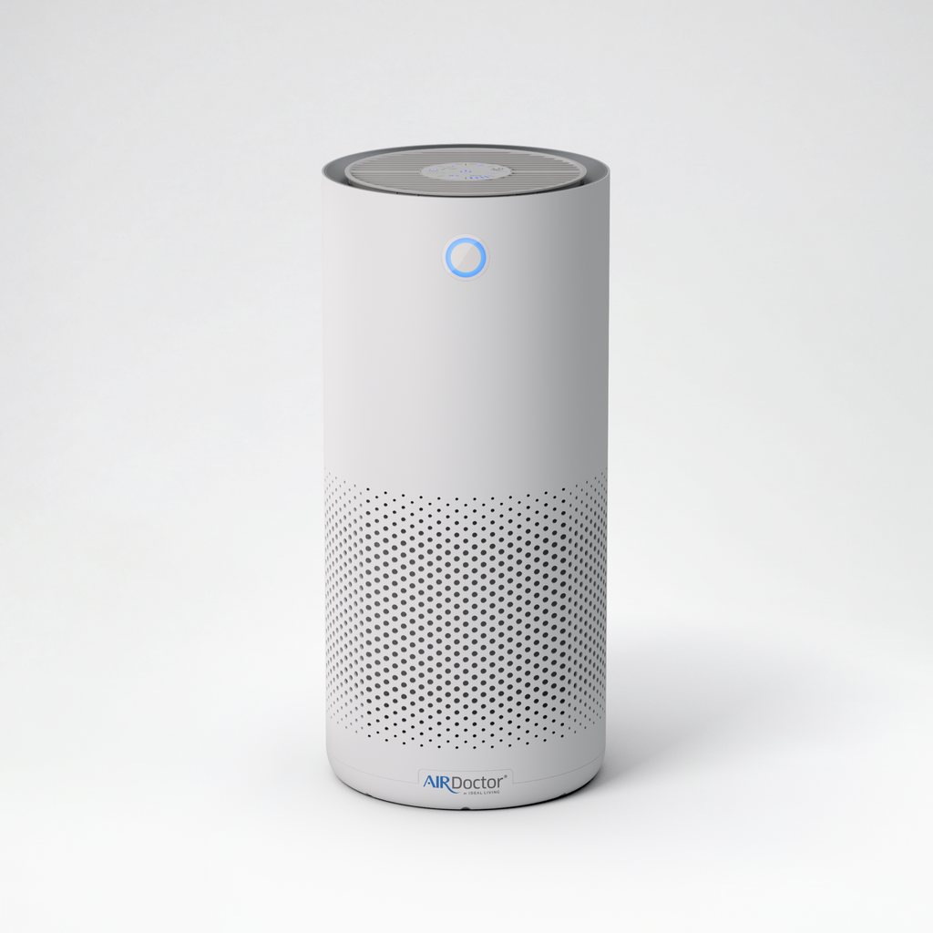 A white cylindrical smart air purifier with a perforated lower grille and a blue indicator light, standing on a light gray background. The brand name 'AIRDoctor' is visible at the bottom.
