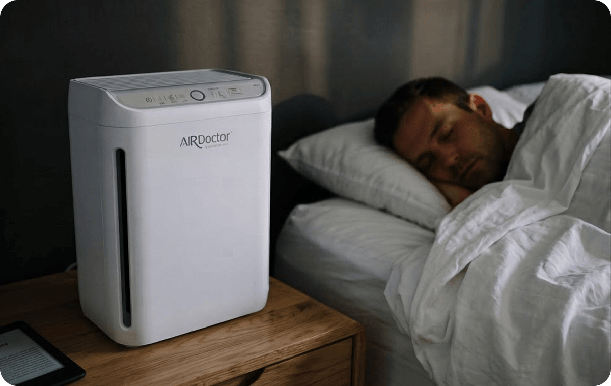 A man asleep in bed next to an AirDoctor GO! on a nightstand