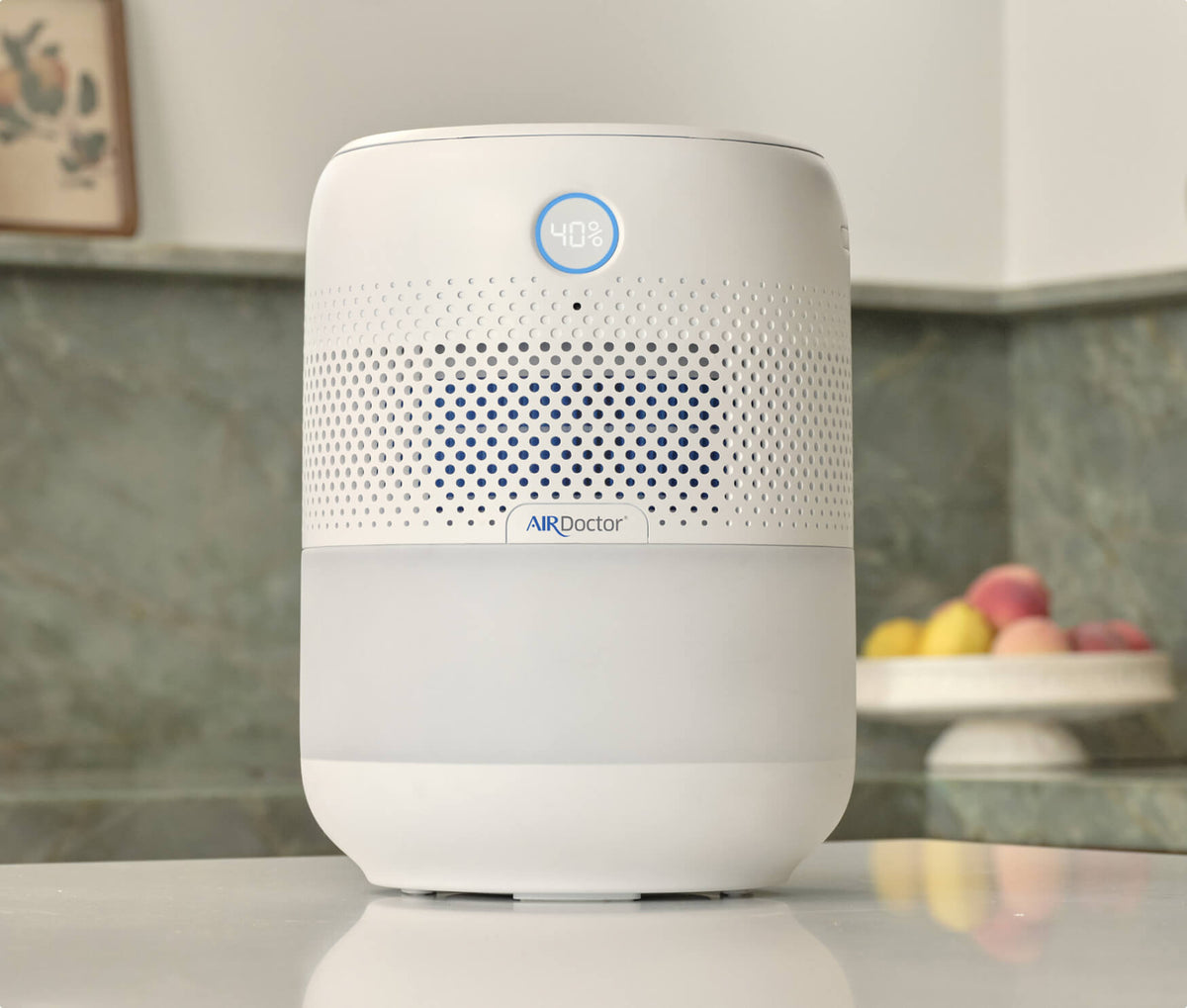 AIRDoctor air purifier on a countertop, displaying a blue indicator light and surrounded by a marble backdrop.