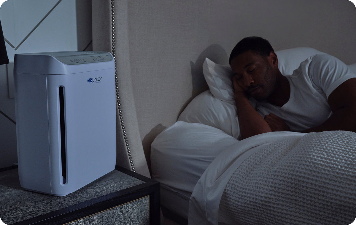 A man in bed sleeping next to an AirDoctor GO!
